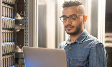 Junger mann mit Laptop steht vor einem Serverrack.