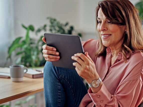 Eine Frau im Homeoffice schaut sich etwas auf einem Tablet an.