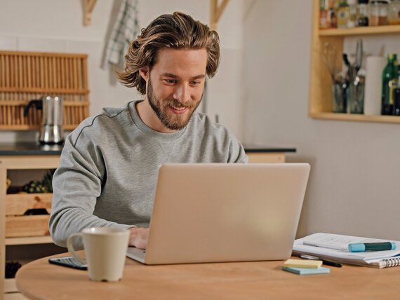Ein Mann sitzt in der Küche und arbeitet an seinem Laptop.