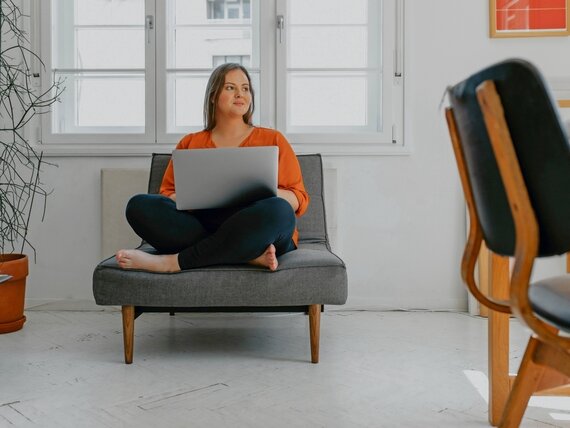 Eine Frau sitzt in einem Sessel mit einem Laptop auf dem Schoß.