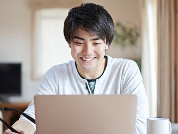 Ein junger Mann sitzt fröhlich vor seinem Laptop.