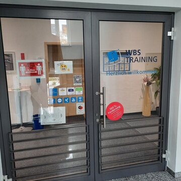 Eingangstür im Treppenhaus Flur. Glastüre mit blauem WBS TRAINING Schriftzug und Logo.