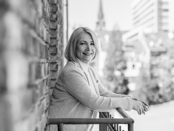 Schwarz-Weiß-Aufnahme einer Frau, die auf einem Balkon steht und sich an das Geländer lehnt