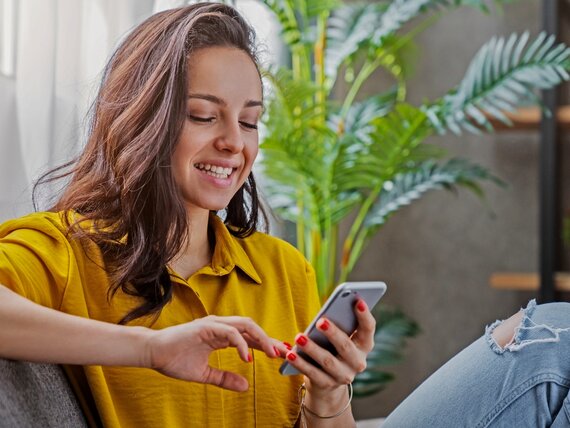 Eine Frau sitzt entspannt auf dem Sofa und benutzt ihr Smartphone.