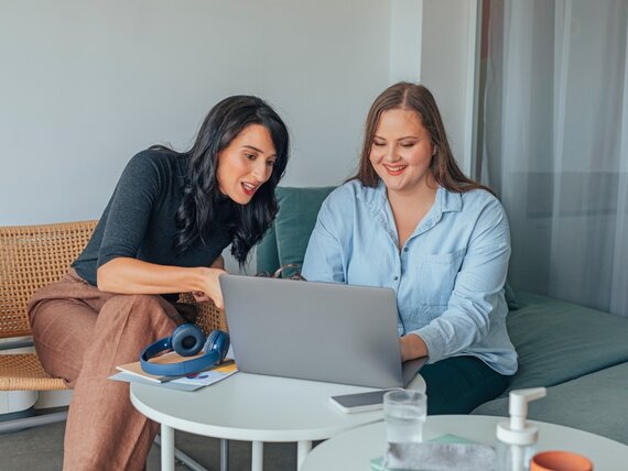 Zwei Frauen arbeiten gemeinsam an einem Laptop.