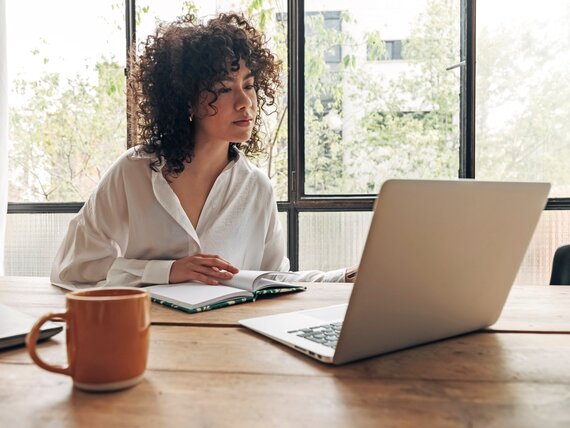 Eine Frau sitzt vor ihrem Laptop und macht sich Notizen.