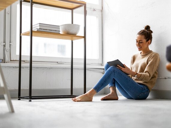 Eine fröhliche Frau mit einem Tablet sitzt entspannt auf dem Boden.