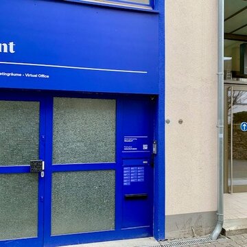 Der Eingangsbereich von außen. Blaue Glastüre mit der Aufschrift Stunt. Im Hintergrund ist der Eingangsbereich eines Fitnessstudios zu sehen.