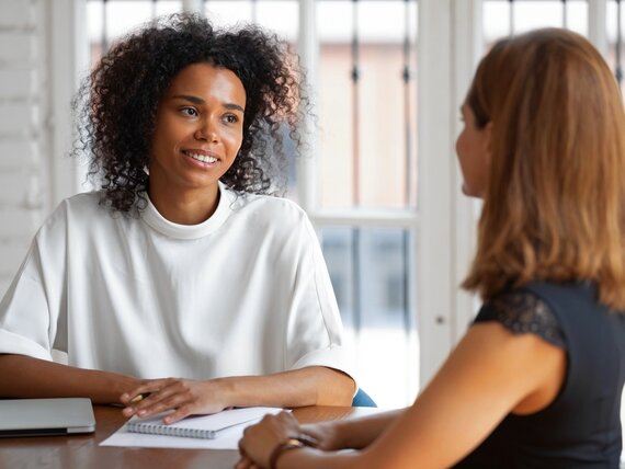 Zwei Frauen unterhalten sich und eine davon macht sich Notizen.