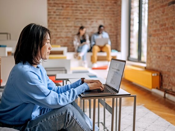 Eine Frau sitzt in einem offenem Büro und arbeitet am Laptop.