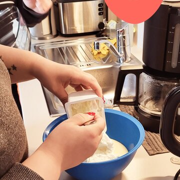 Eine Teilnehmerin beim Backen am Standort. Schüssel mit Mehl. Darüber ein Herz mit einem lächelnden Gesicht.