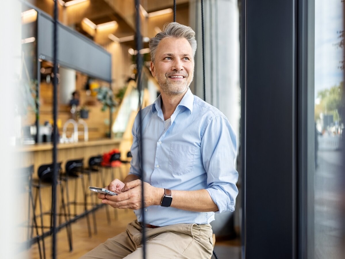 Ein Mann steht in einer Café Bar mit seinem Smartphone und schaut aus dem Fenster