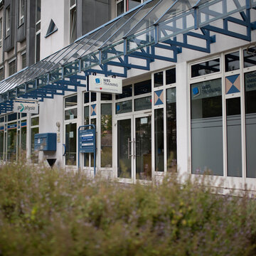 Außenansicht des Gebäudes. Glasfront mit blauem Überdachungsgestell. Schild mit der Aufschrift WBS TRAINING – Unser Herz schlägt für Bildung.