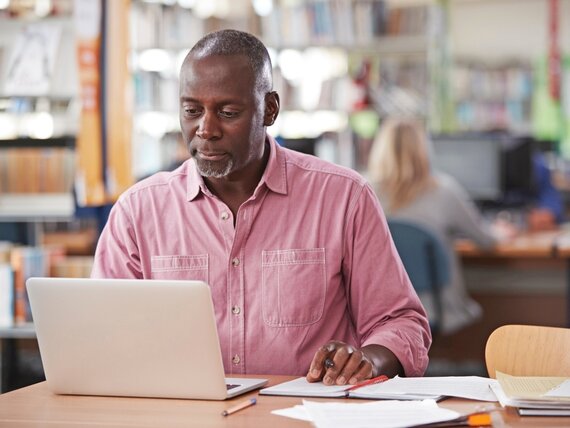 Ein Mann in der Bibliothek, der an seinem Laptop arbeitet.