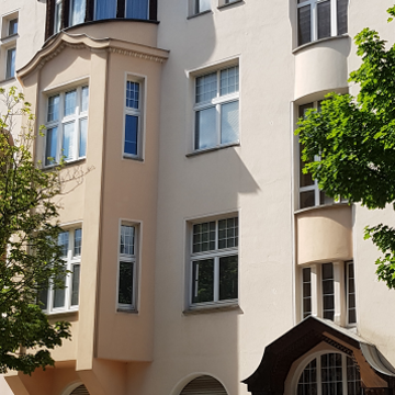Gelbes Gebäude mit Vorsprung und Überdachter Eingangstür. Davor parkt ein Auto.