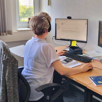 Eine Teilnehmerin sitzt an ihrem Arbeitsplatz und trägt ihr Headset während sie in der virtuellen Lernumgebung lernt.