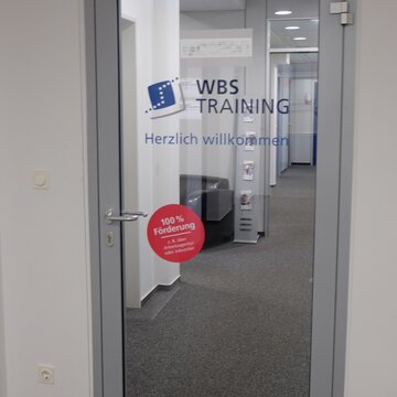 Eine Glastür mit der Aufschrift "WBS TRAINING" und "Herzlich Willkommen".