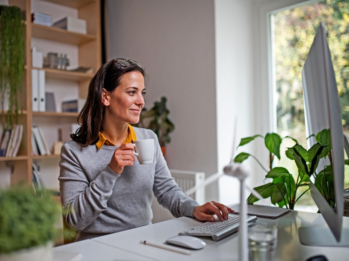 Eine Frau sitzt vor ihrem Computer und hält eine Kaffeetasse in der Hand.