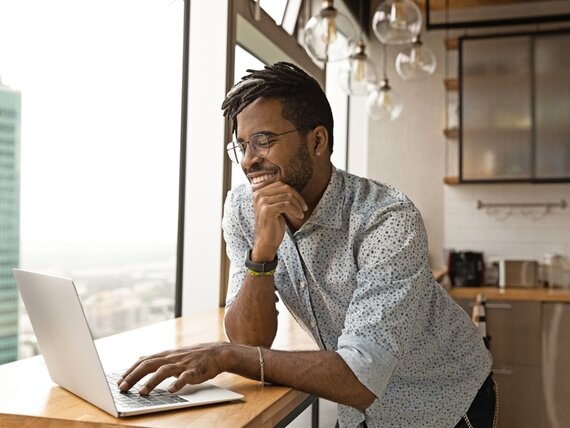 Ein Mann steht in der Küche und arbeitet an seinem Laptop.