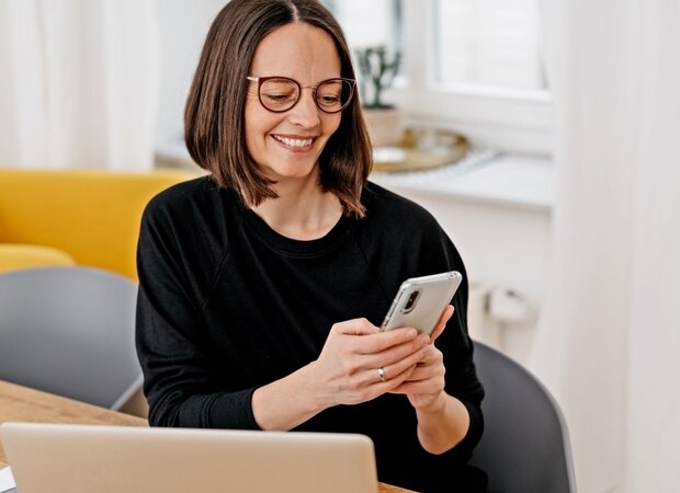 Eine Frau im Homeoffice mit Laptop und Smartphone.