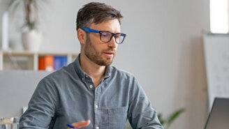 Mann mit Brille und Hemd sitzt an einem Tisch und arbeitet an einem Laptop