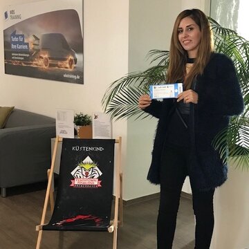 Eine Frau steht neben einem Strandstuhl und hält eine Eintrittskarte in der Hand. Gewinnspiel für Umschüler "Eishockeykarten"