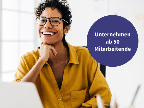 Frau mit Brille lächelt mit aufgestütztem Arm am Laptop.