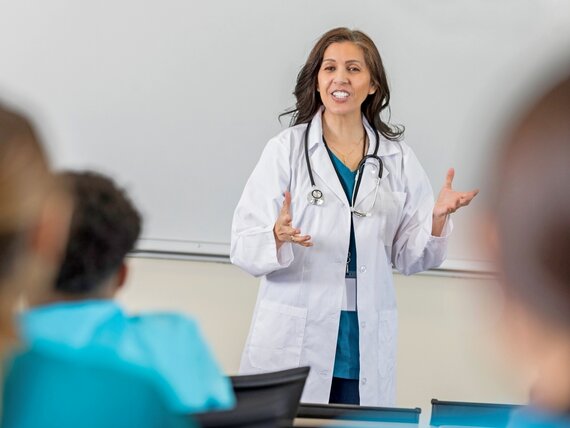 Eine Ärztin steht in einem Schulungsraum und hält einen Vortrag für Schüler und Schülerinnen