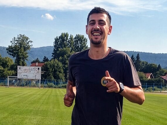 Lachender Mann in schwarzem T-Shirt joggt auf einem Fußballfeld