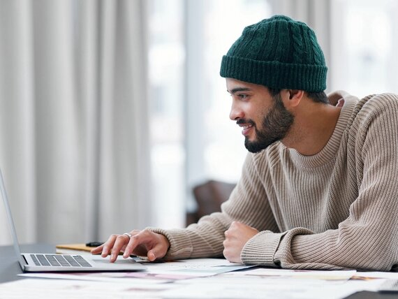 Ein Mann mit Mütze sitzt vor seinem Laptop im Homeoffice.