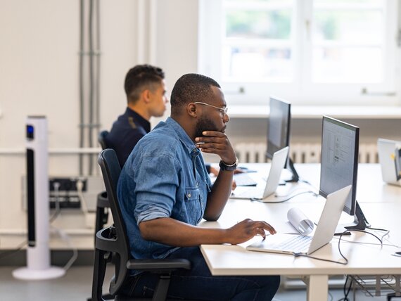 Zwei Männer sitzen nebeneinander an einem Schreibtisch und arbeiten an ihren Laptops.