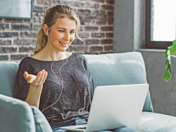 Eine Frau sitzt mit ihrem Laptop auf dem Sofa und nimmt an einer Videokonferenz teil.