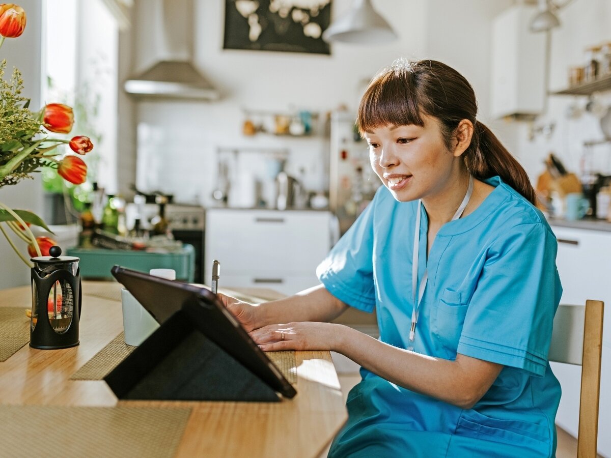 Eine Frau sitzt mit einem Tablet in der Küche und macht sich Notizen.