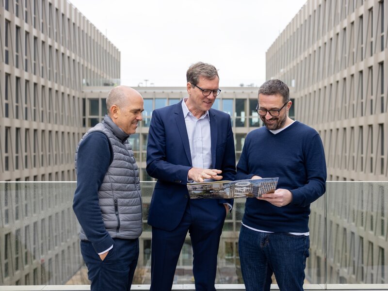 Drei Männer stehen auf einer Büroterrasse und betrachten gemeinsam Unterlagen.