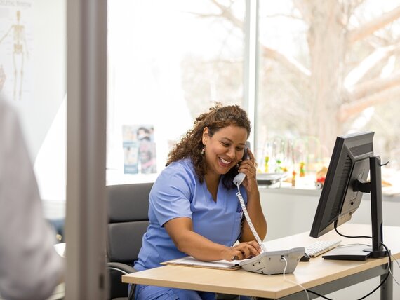 Eine fröhliche medizinische Fachangestellte sitzt in einem Büro und telefoniert