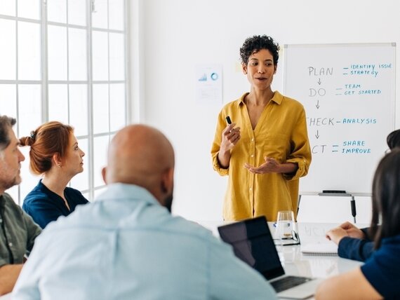 Eine Frau steht vor einem Flipchart und präsentiert vor einem mehrköpfigen Team