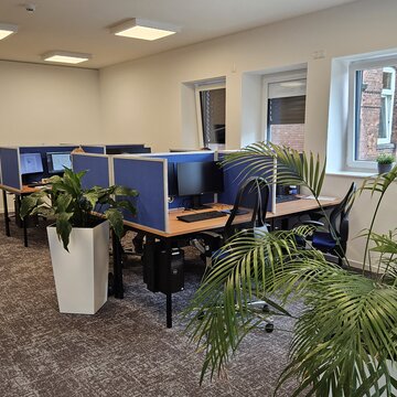 Schulungsraum mit mehreren Arbeitsplätzen mit jeweils 2 Bildschirmen, einem Bürostuhl, Tastatur und Maus. Im Raum mehrere Topfpflanzen