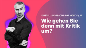 Mann mit kurzem Haar und Bart in schwarzem Hemd mit verschränkten Armen und hochgezogener Augenbraue, fragender Blick