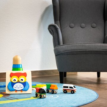 Kinderecke mit einem türkisen Teppich und Spielzeug. Dahinter ein grauer Kindersessel.