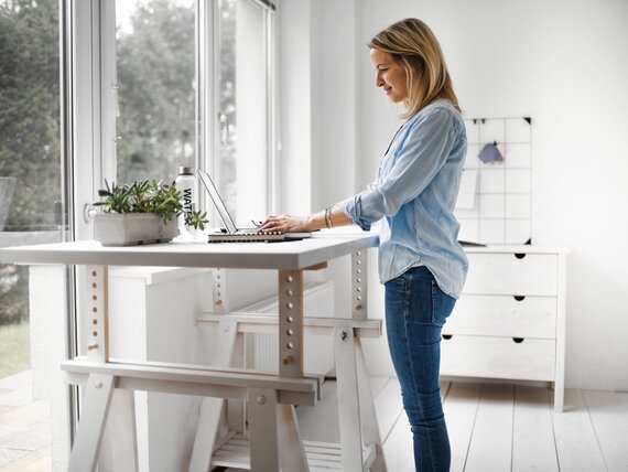 Eine Frau steht vor ihrem Schreibtisch und arbeitet am Laptop.
