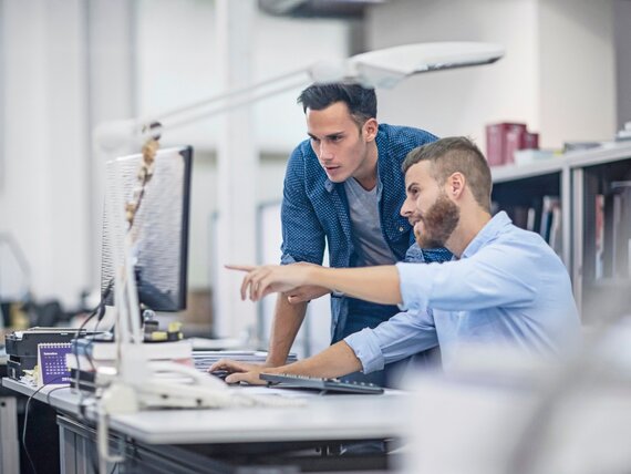 Zwei Männer im Büro sehen sich etwas auf einem Computer Bildschirm an