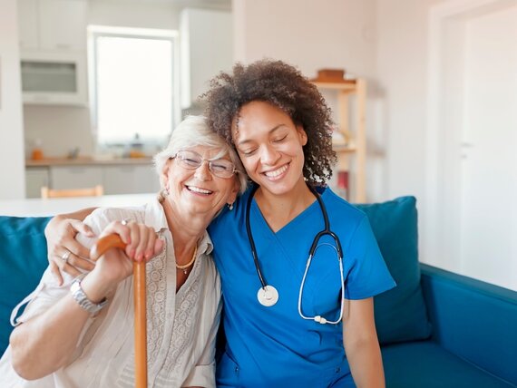 Eine junge Pflegerin umarmt eine Seniorin herzlich