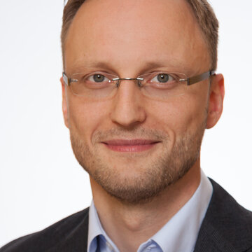 Mann mit Brille und braunem Haar schaut freundlich.