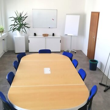 Heller Konferenzraum mit großem Tisch und 10 Stühlen. Blick auf die Wand, an der ein Whiteboard über einem weißen Sideboard hängt. Daneben steht ein Flipchart und auf dem Sideboard steht eine grüne Zimmerpflanze.