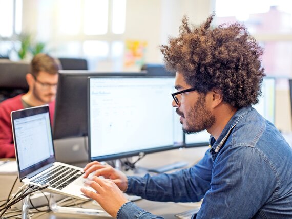 Ein Mann sitzt vor mehreren Bildschirmen und arbeitet an seinem Laptop.