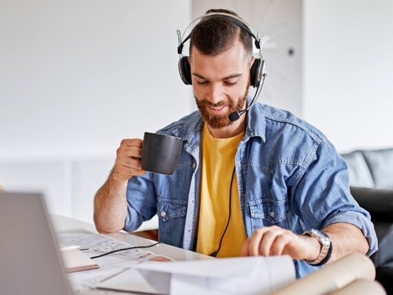 Ein Mann mit Headset arbeitet an seinem Schreibtisch und trinkt einen Kaffee.