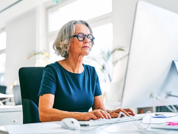 Eine Frau im mittleren Alter bei der Arbeit vor einem Computerbildschirm.