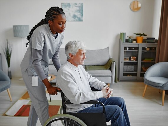 Eine Pflegerin kümmert sich um einen Senior im Rollstuhl