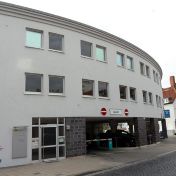 Außenansicht des Gebäudes, Halbrunde Form und helle Fassade. Im Erdgeschoss befindet sich ein Parkhaus.