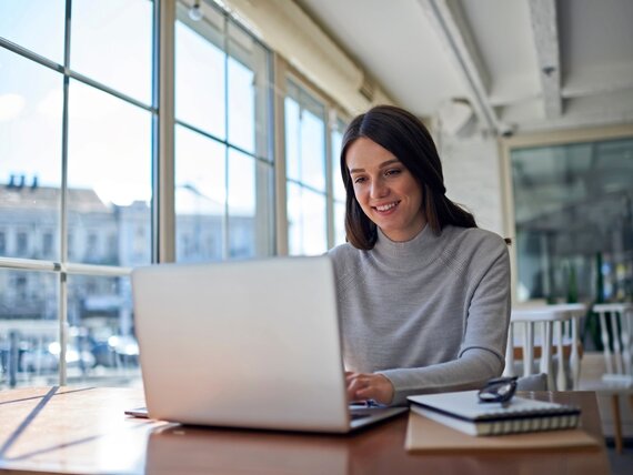 Eine Frau arbeitet am Laptop in einem Büro mit großem Fenster.
